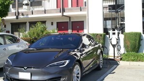 Una Tesla Model S parcheggiata di fronte a un edificio con porte rosse e una scalinata.