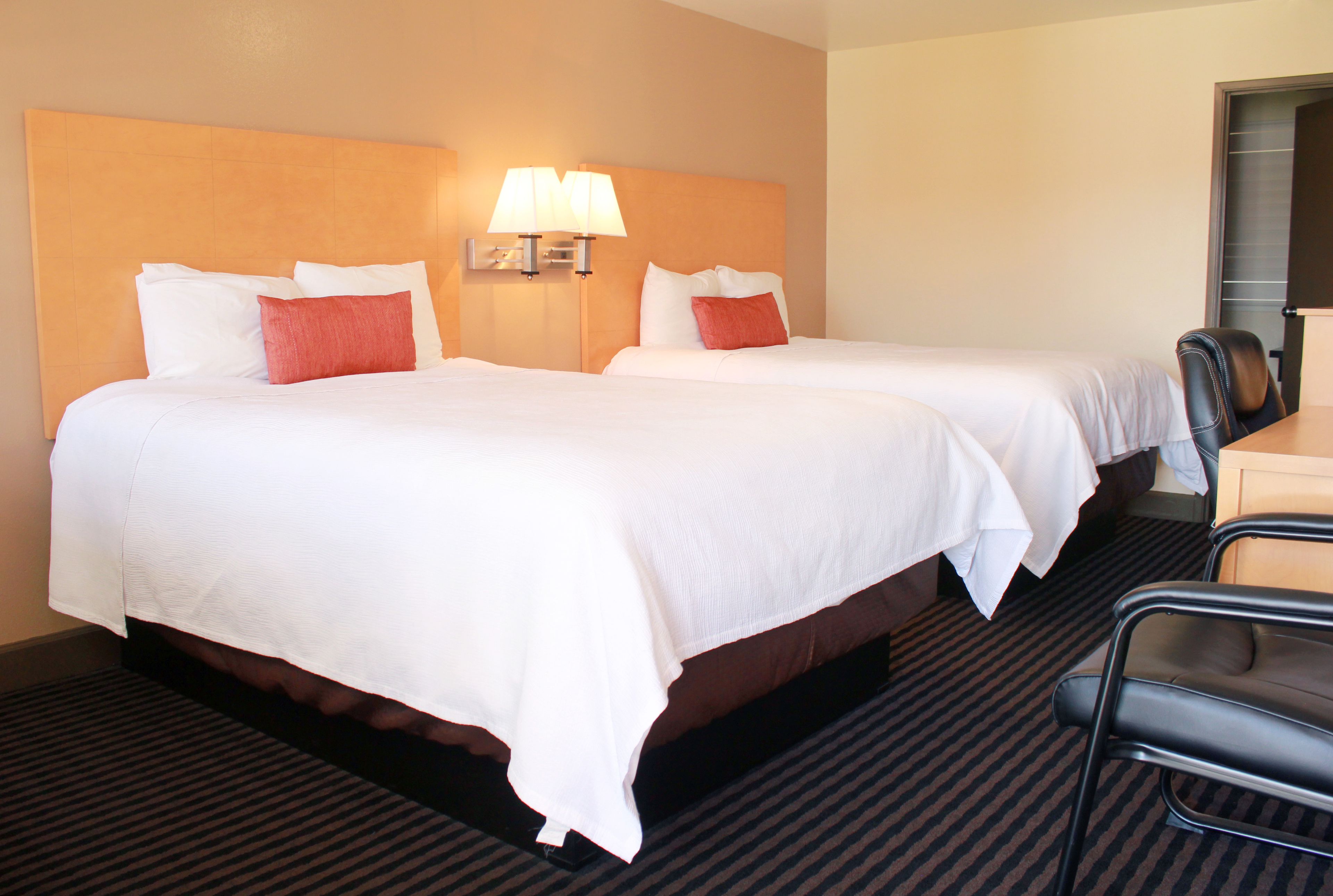 A hotel room with two beds, a desk, and a chair.