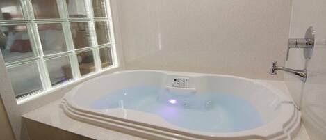 A modern bathroom with a freestanding bathtub, a window with frosted glass, and a white tiled wall.