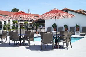 An outdoor pool area with multiple tables and chairs, surrounded by red and white patterned umbrellas, and a building with a tiled roof in the background. - Travelodge by Wyndham Vallejo (Vallejo)