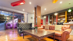 A spacious lobby with a wooden floor, leather sofas, a coffee table, and a staircase in the background. - Madam Inn Patong (Patong)