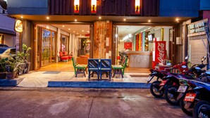 A hotel entrance with a Coca-Cola sign, outdoor seating, and parked motorcycles. - Madam Inn Patong (Patong)
