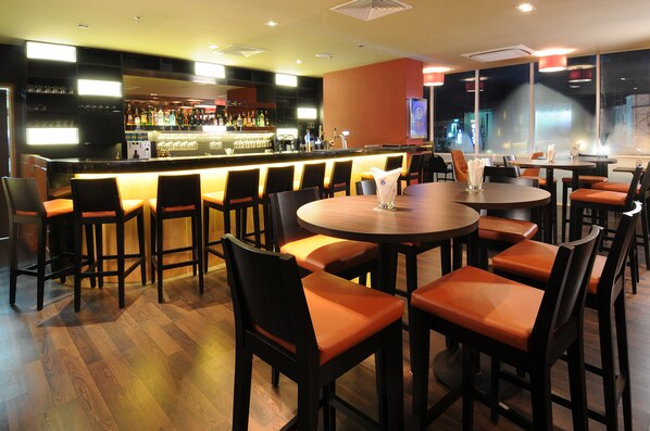 Uma área de bar com diversas opções de assento, incluindo banquetas e mesas, além de um balcão com diversos tipos de garrafas e copos.