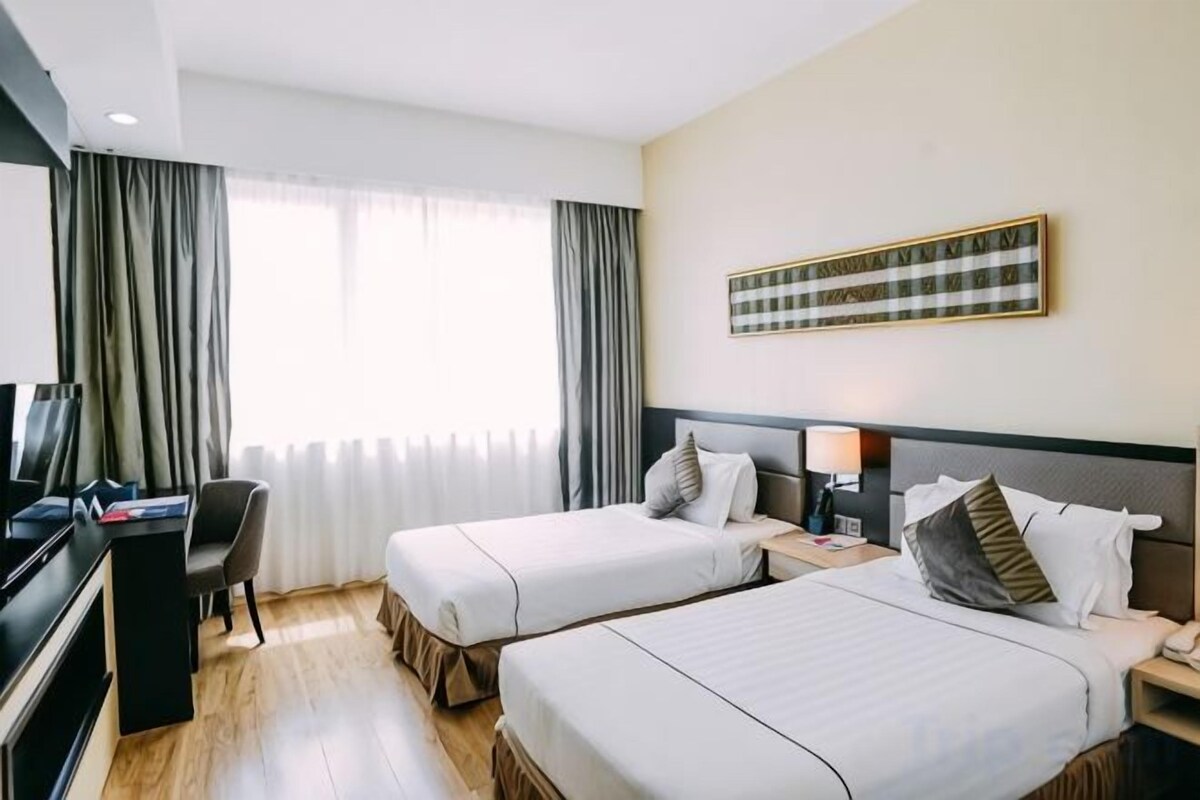 Ein Hotelzimmer mit zwei Betten, einem Schreibtisch, einem Fernseher und einem großen Fenster mit Vorhängen.