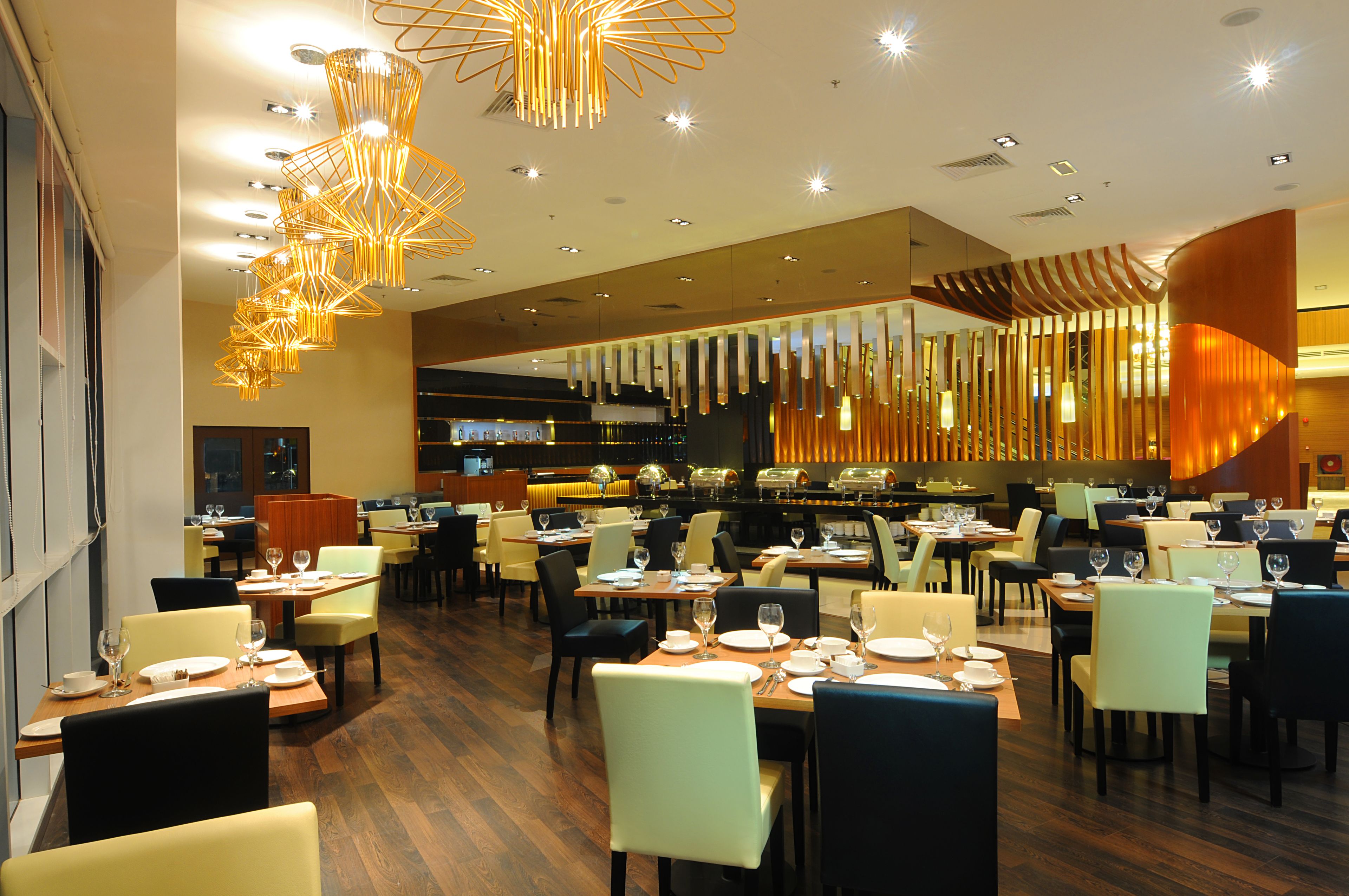 A modern restaurant with multiple dining areas, wooden flooring, and contemporary lighting fixtures.