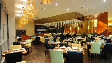 A modern restaurant with multiple dining areas, wooden flooring, and contemporary lighting fixtures.