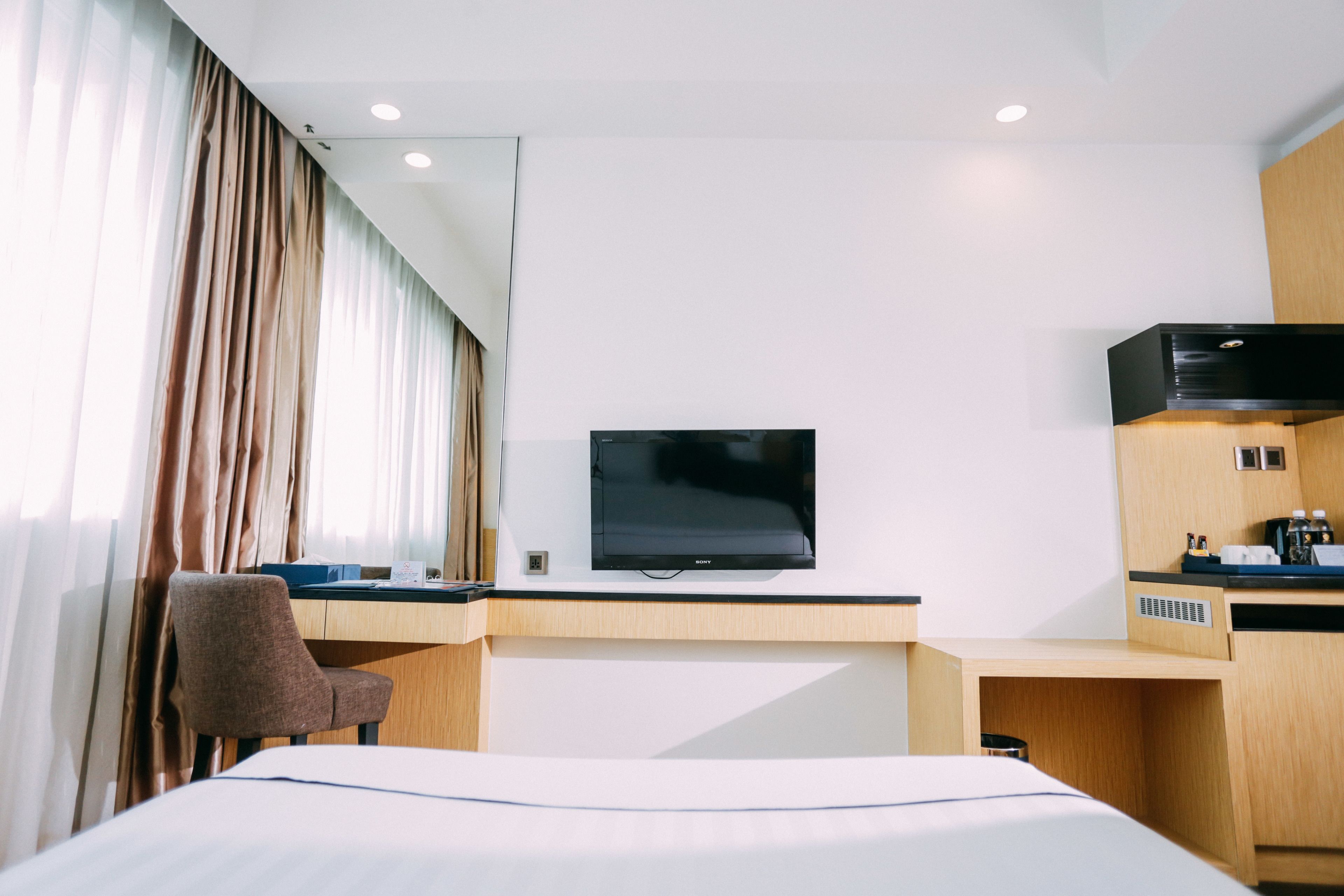 A hotel room with a bed, a desk, a chair, a television, and a minibar.