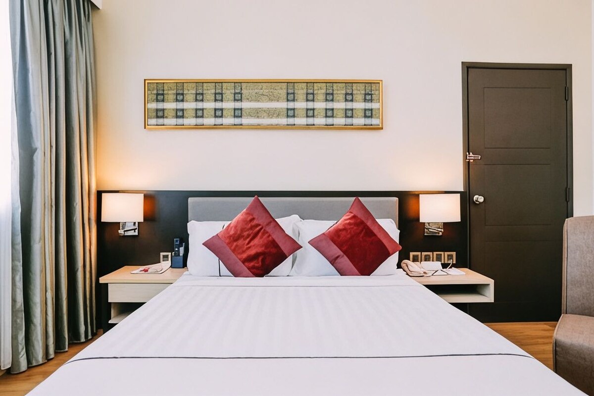 Habitación de hotel con una cama grande, dos lámparas de noche, una puerta y una obra de arte enmarcada en la pared.
