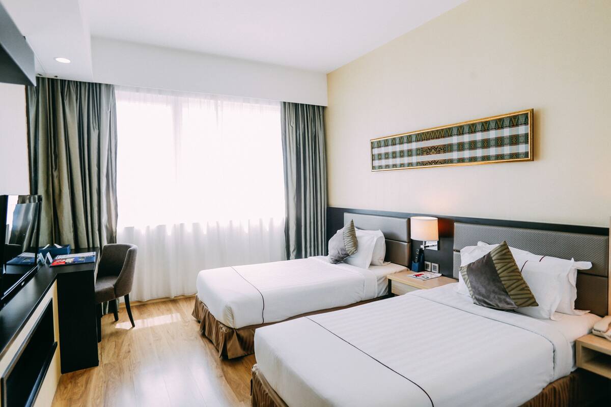 A hotel room with two beds, a desk, and a television.
