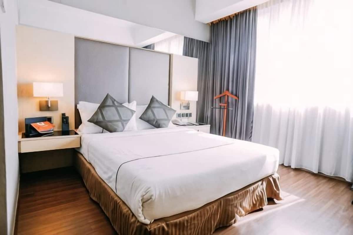 A hotel room with a large bed, bedside tables, a desk, and a wardrobe.