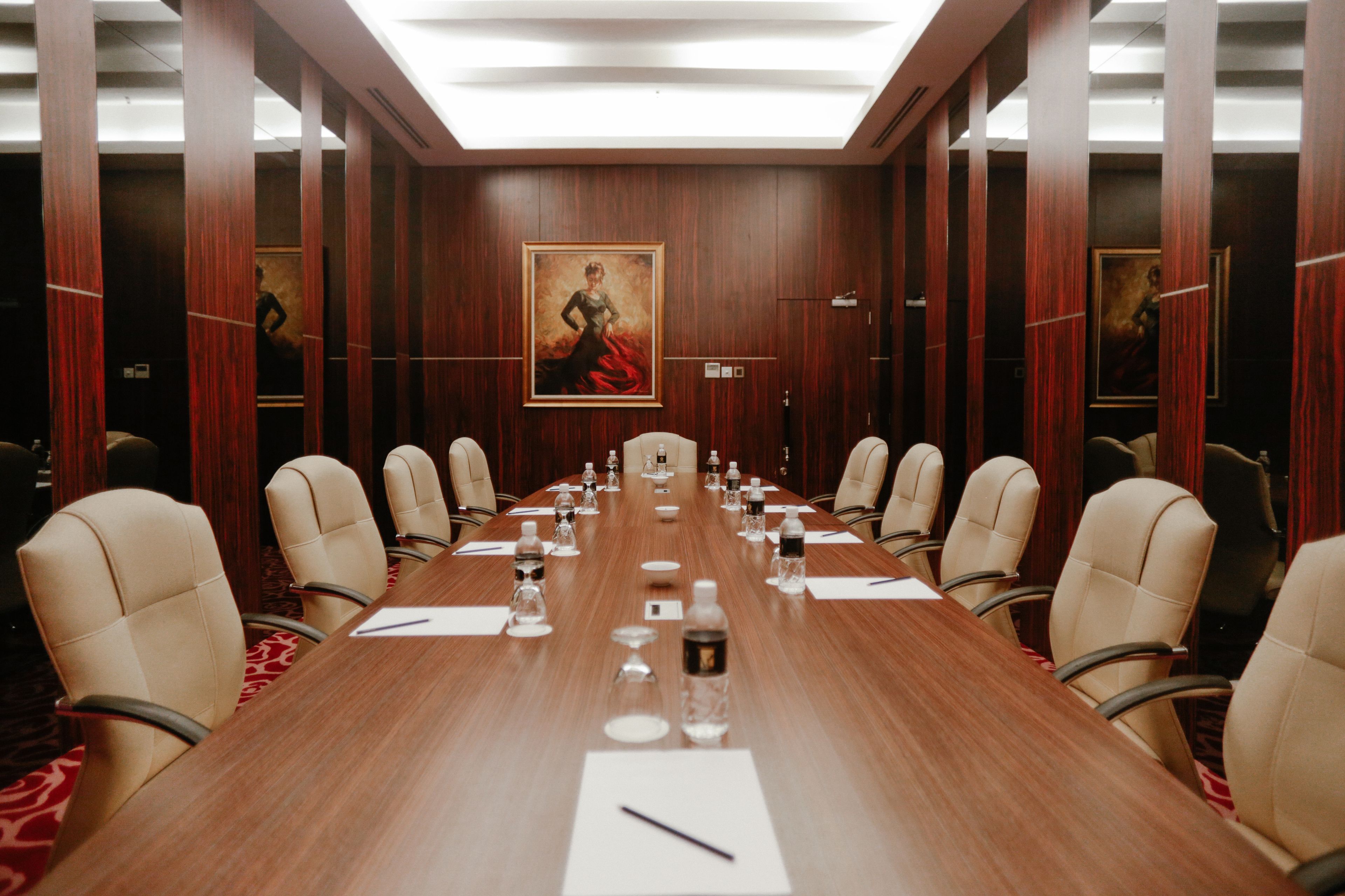 A conference room with a long wooden table, beige chairs, and a painting on the wall.