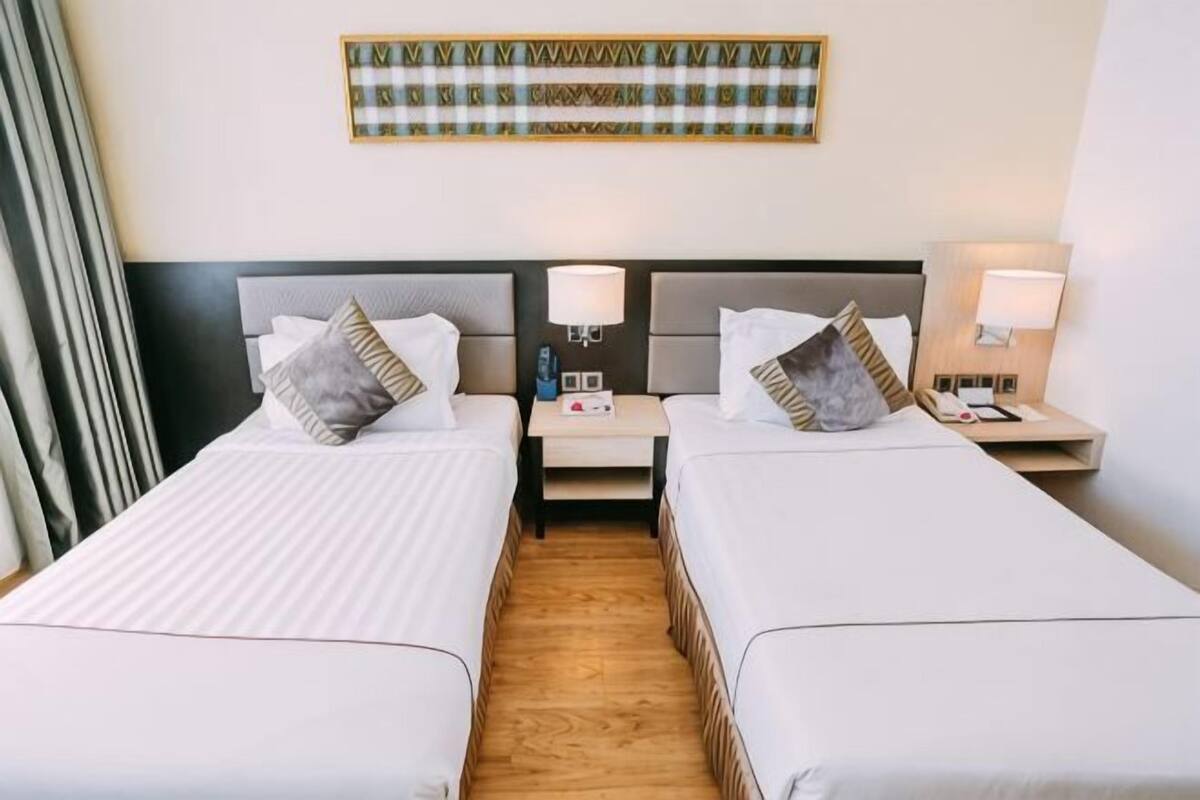 A hotel room with two beds, nightstands, lamps, and a decorative wall piece.