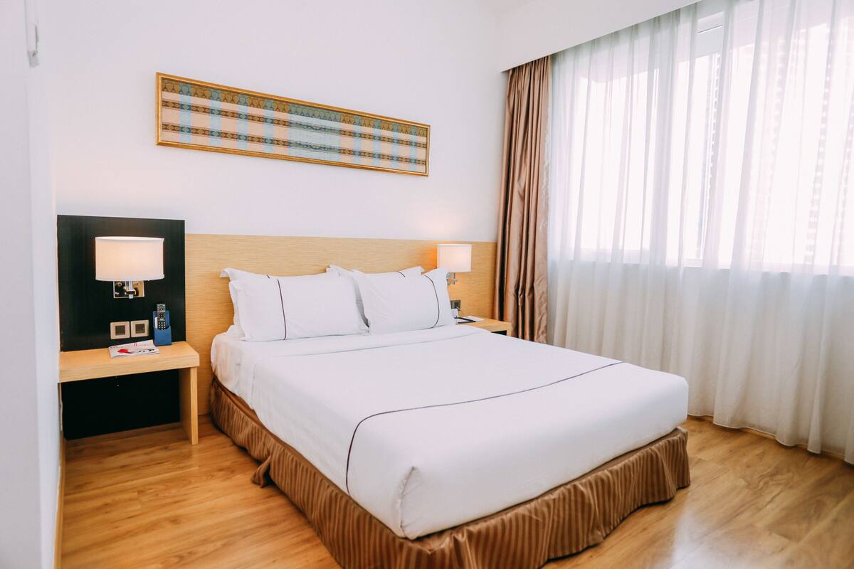 A hotel room with a large bed, two bedside tables with lamps, a remote control, and a wall-mounted artwork.