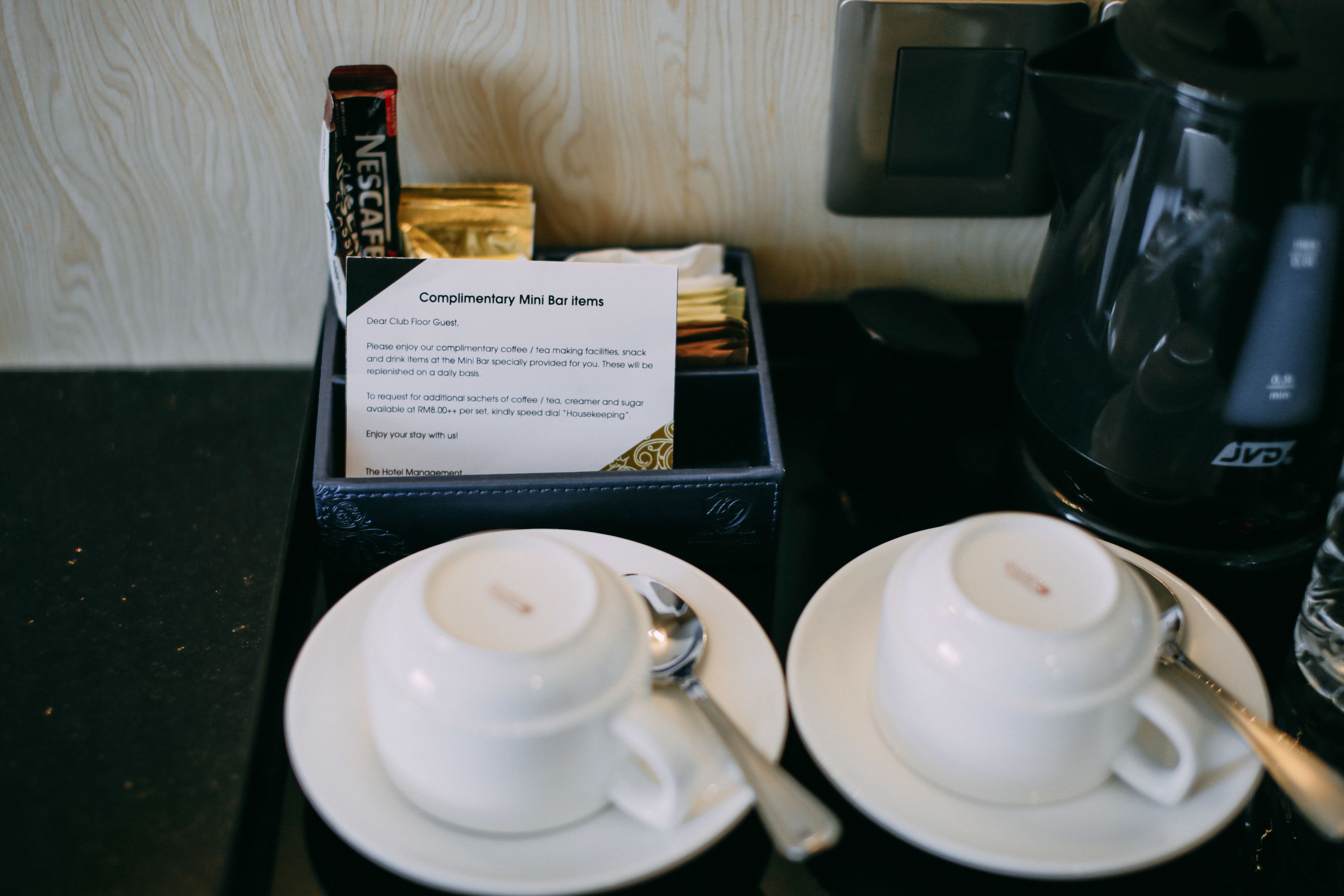 En minibar med ett urval av drycker och snacks ingår, tillsammans med två vita koppar och skedar, en kaffebryggare från Nescafé och en skylt som beskriver vilka produkter som finns tillgängliga.