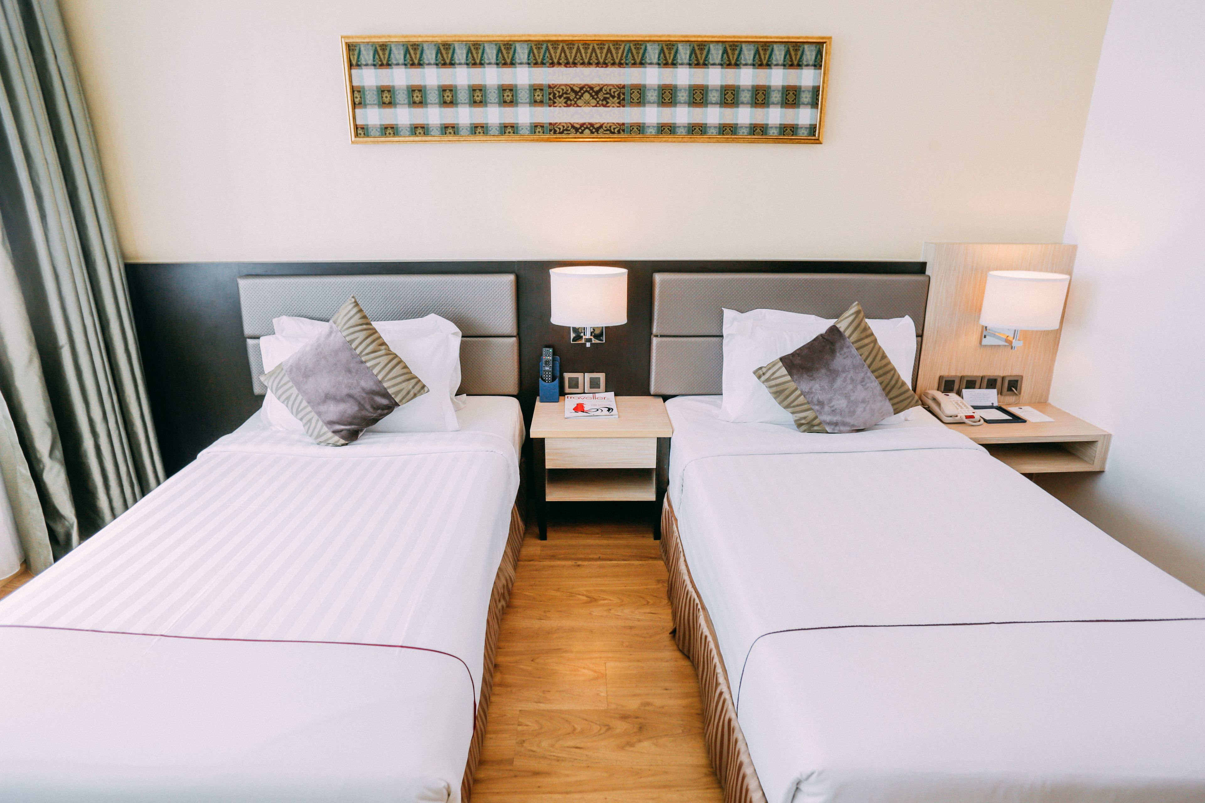 Habitación de hotel con dos camas individuales, una mesita de noche con lámpara, teléfono y una obra de arte enmarcada en la pared.