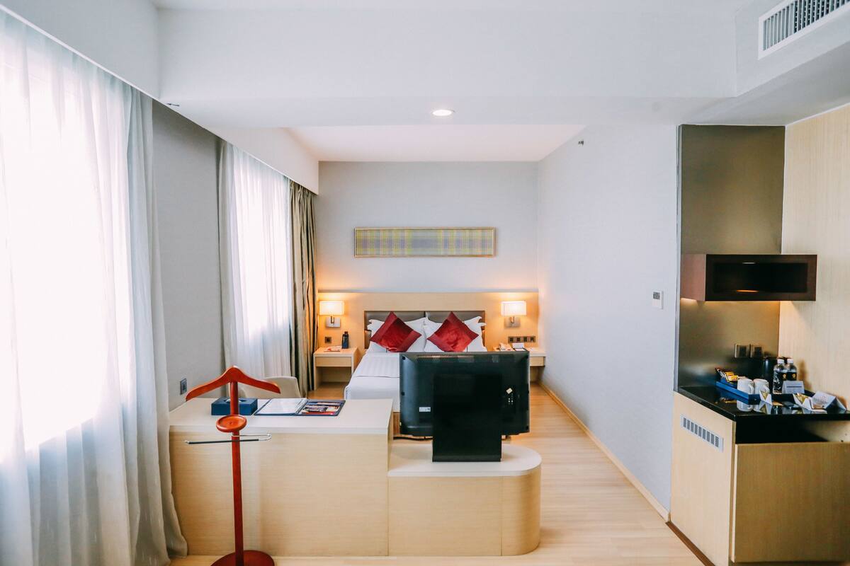 A hotel room with a bed, a desk, a TV, and a minibar.