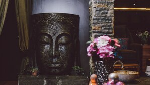 Una estatua de Buda, un florero con flores y una pequeña figurita de Buda sobre una mesa de madera.