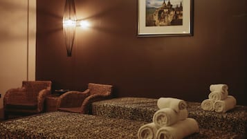 Um quarto de spa com carpete estampado, duas cadeiras de vime, um quadro na parede e toalhas enroladas no chão.