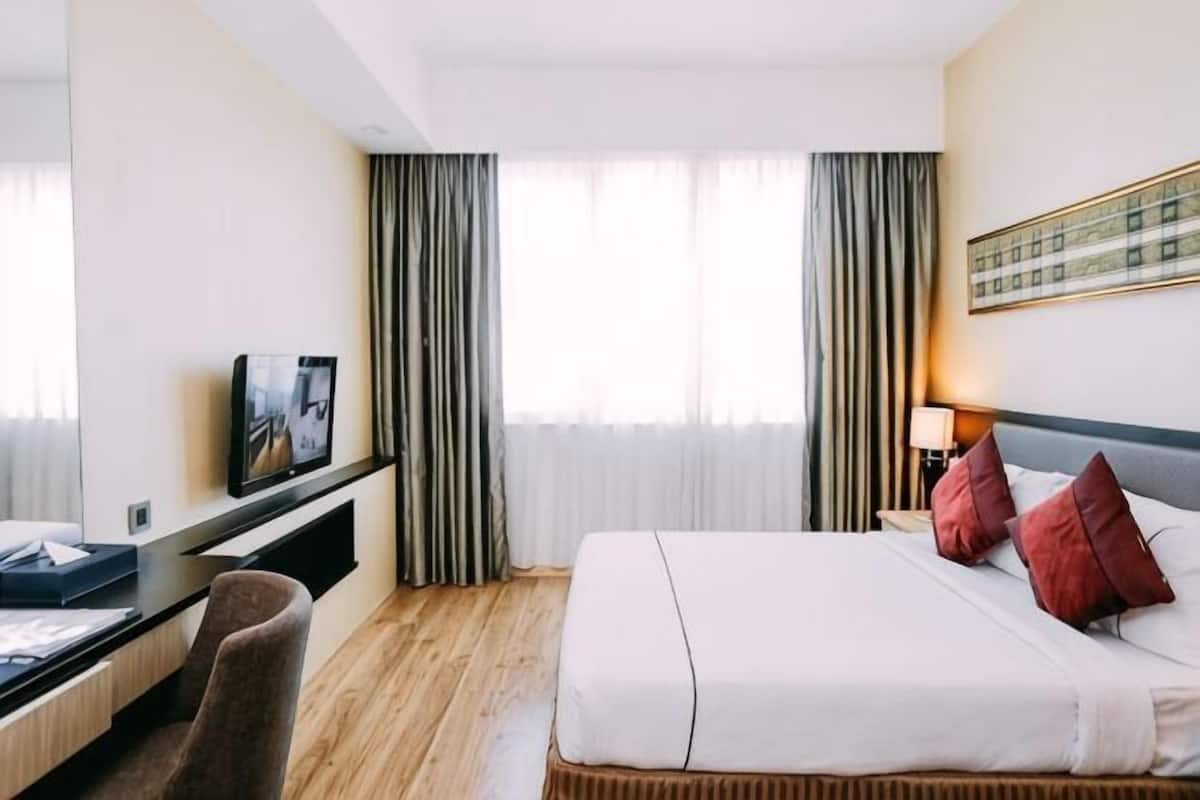 A hotel room with a bed, a desk, a chair, a TV, and a window with curtains.