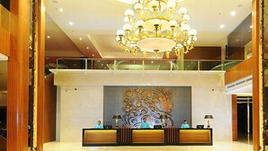 Un vestíbulo de hotel con mostrador de recepción, una lámpara de araña grande y un mural decorativo.