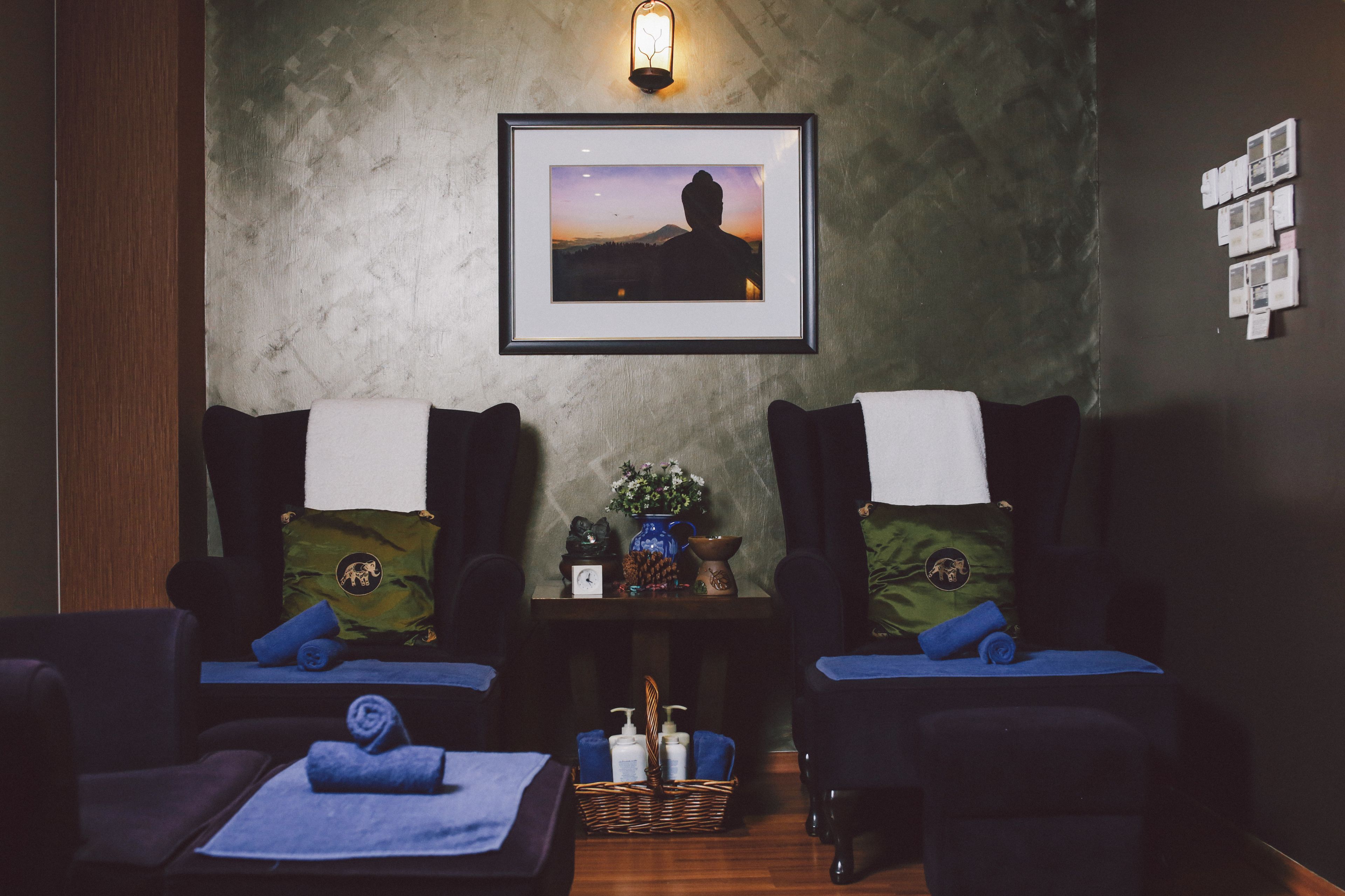 Une salle de spa équipée de deux fauteuils de massage, d’un tableau encadré au mur, d’une petite table avec un vase et des objets décoratifs, et d’un panier contenant des bouteilles.