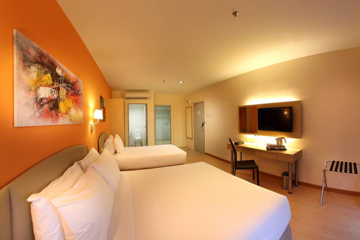 A hotel room with two beds, a desk, a chair, a TV, and a painting on the wall.