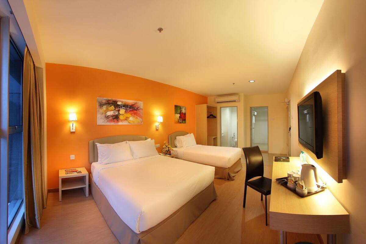 A hotel room with two beds, a desk with a chair, a television, and artwork on the walls.