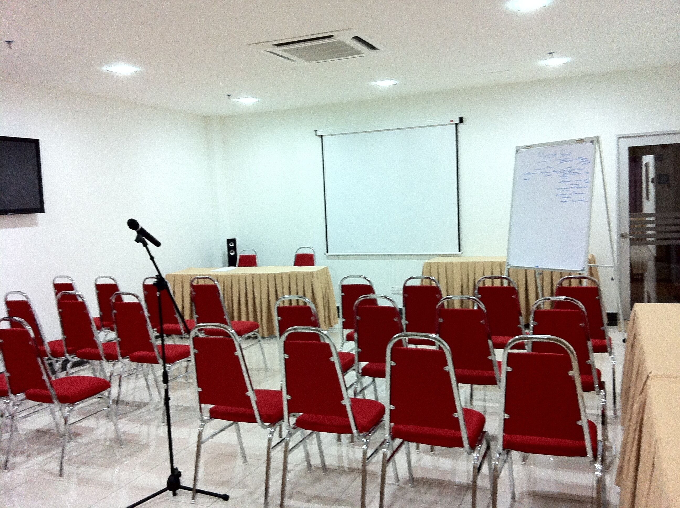 Une salle de conférence avec des chaises rouges, une table, un écran de projection et un tableau blanc.
