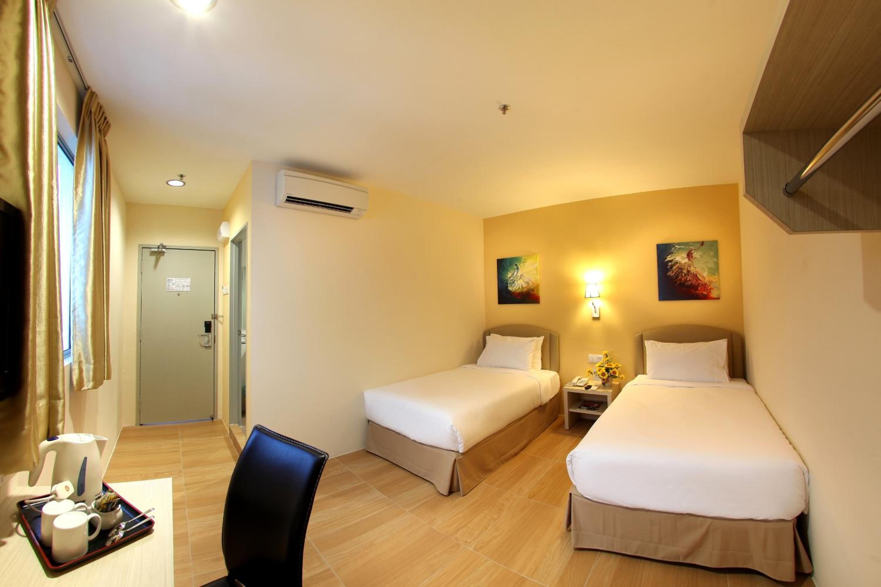 Une chambre d’hôtel avec deux lits simples, un bureau avec une chaise, une petite table avec un plateau contenant des articles pour le petit-déjeuner et deux lampes fixées au mur.