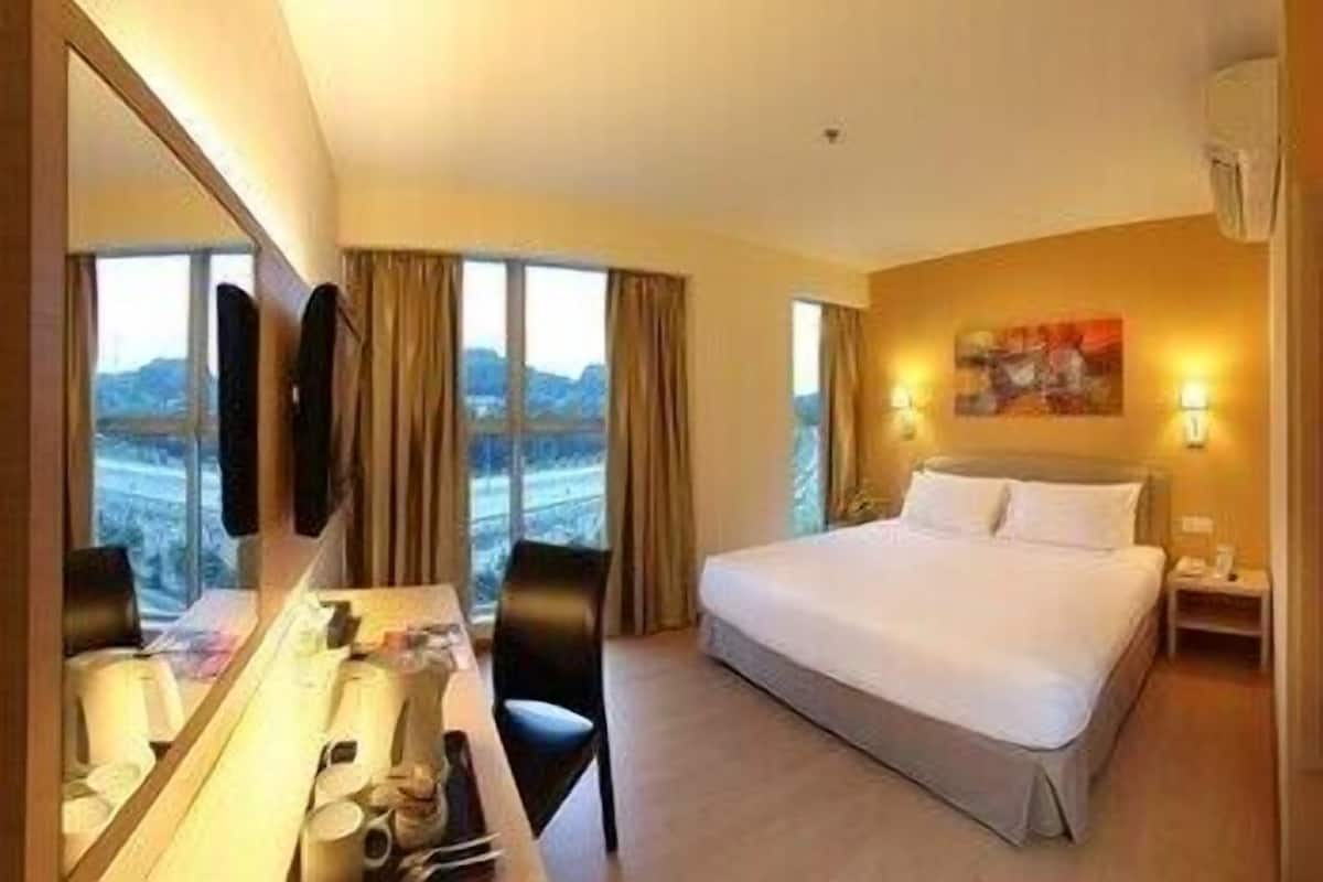 A hotel room with a bed, a desk, a chair, a large window, and a painting on the wall.