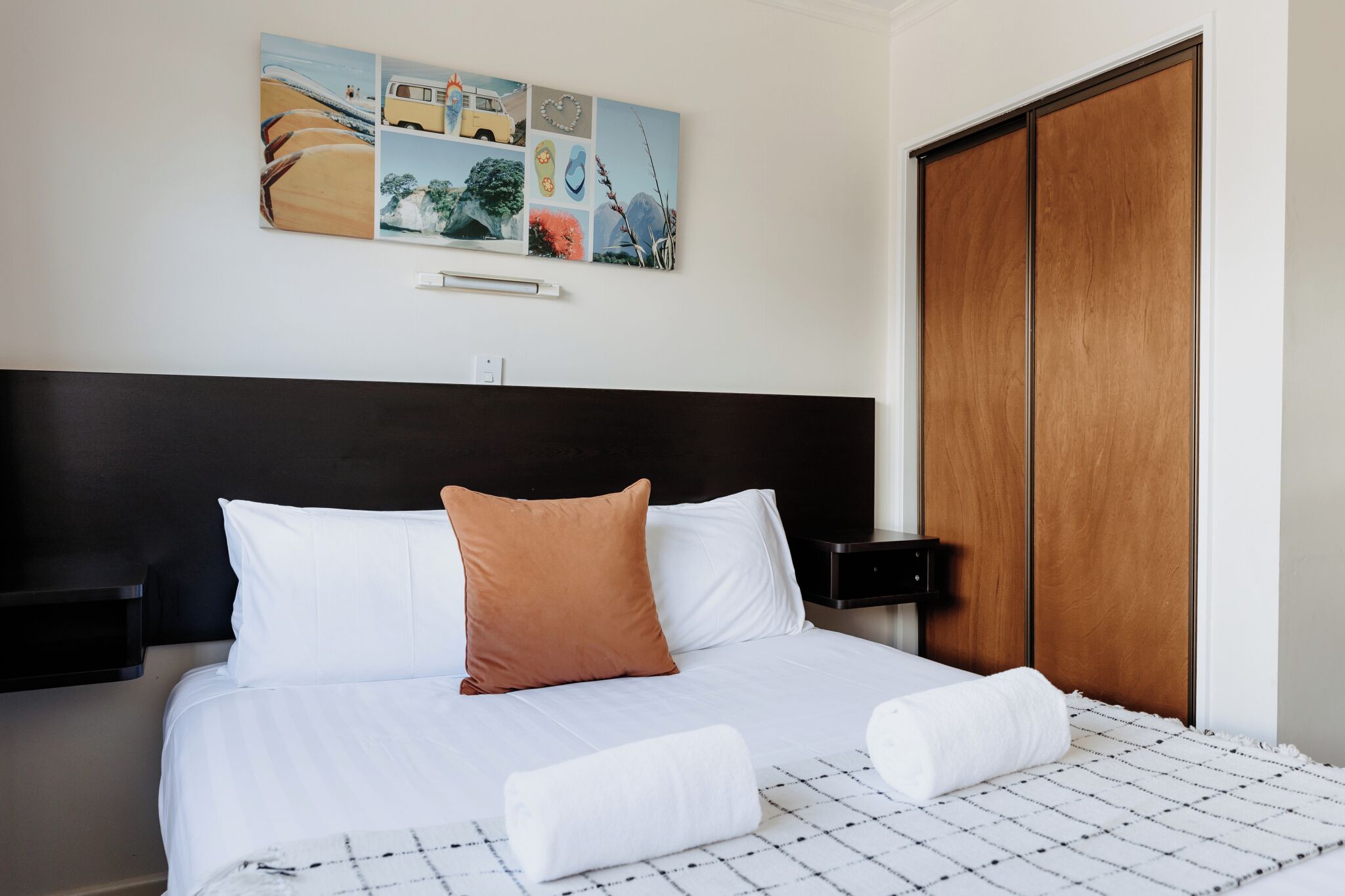 A neatly made bed with white and brown pillows, a black headboard, and a wooden wardrobe.