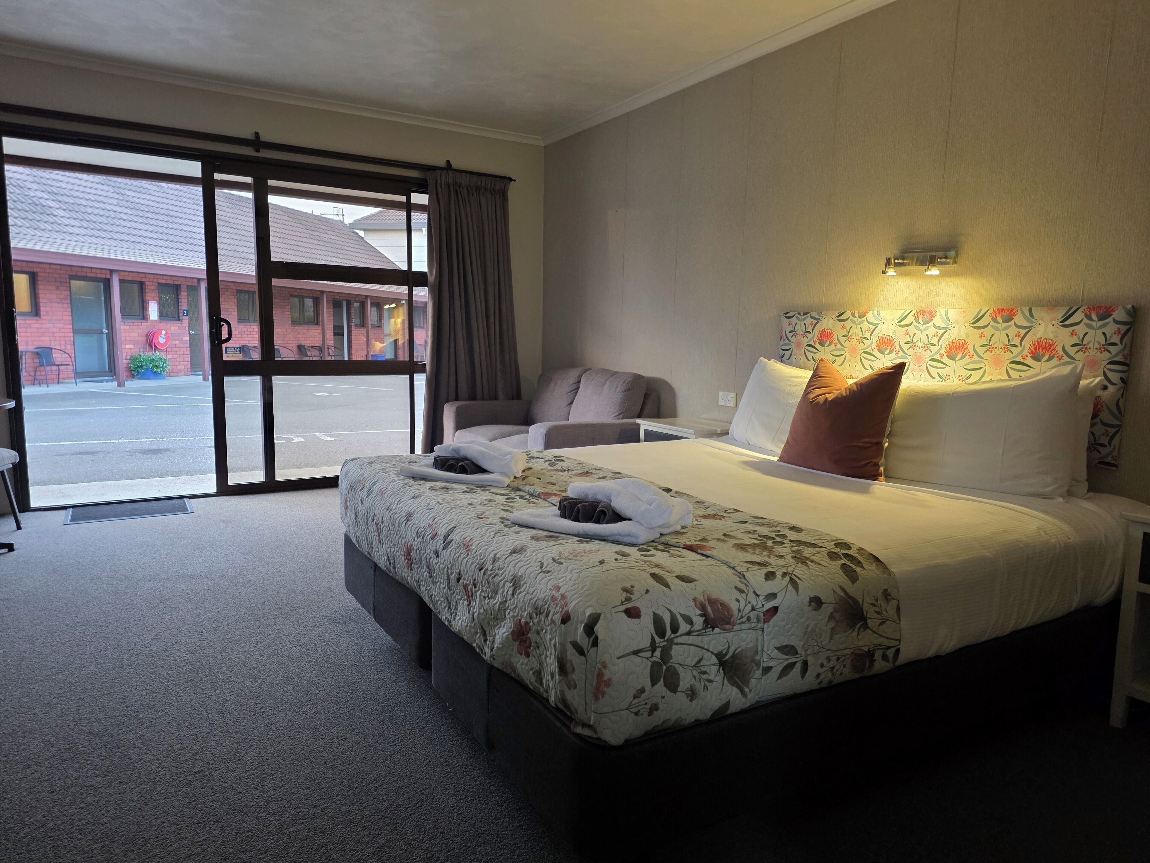 Habitación de hotel con una cama grande, una silla, un escritorio y vistas a la calle a través de una puerta corredera.