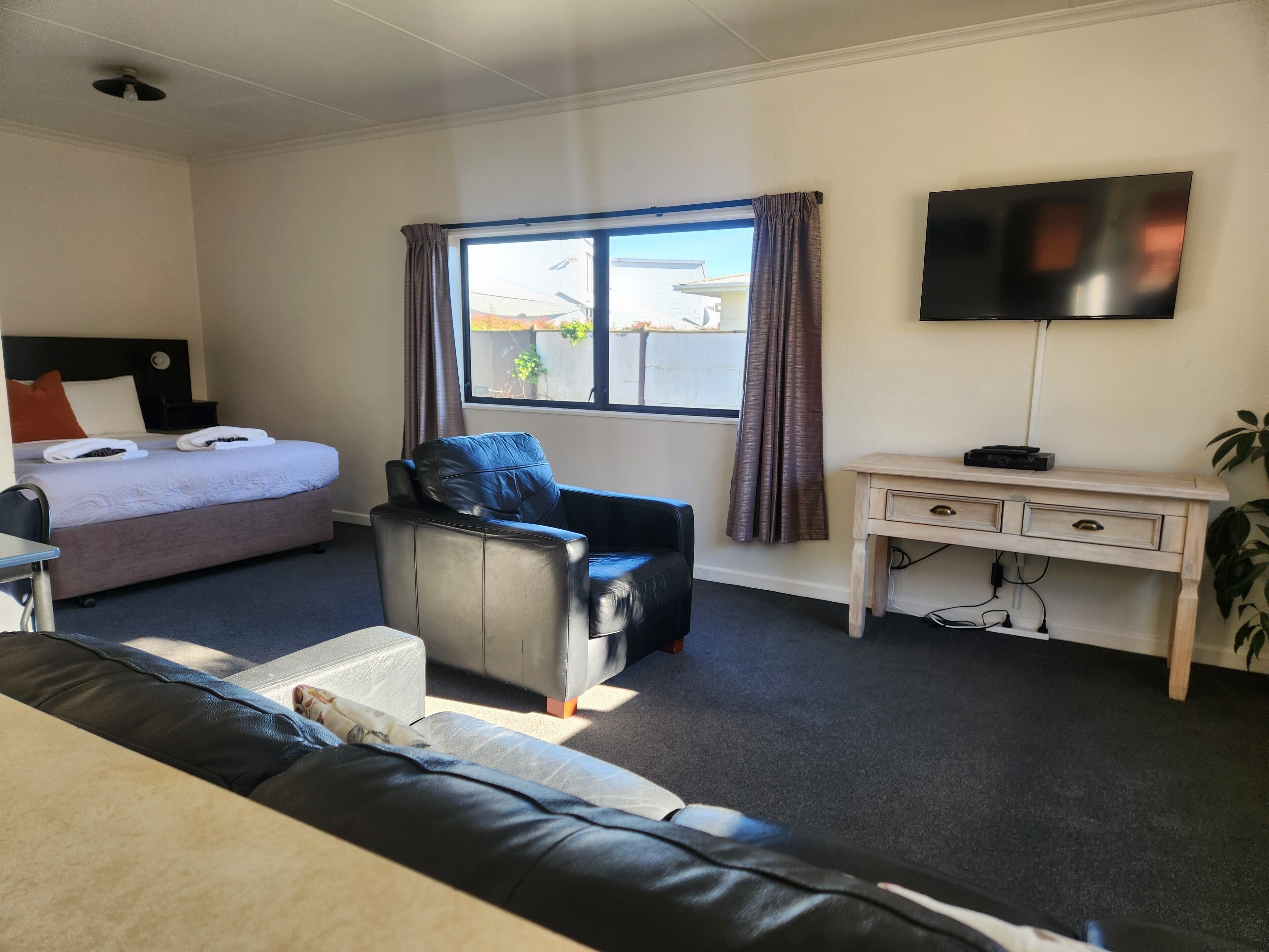 A hotel room with a bed, a desk, a chair, a TV, and a window with curtains.