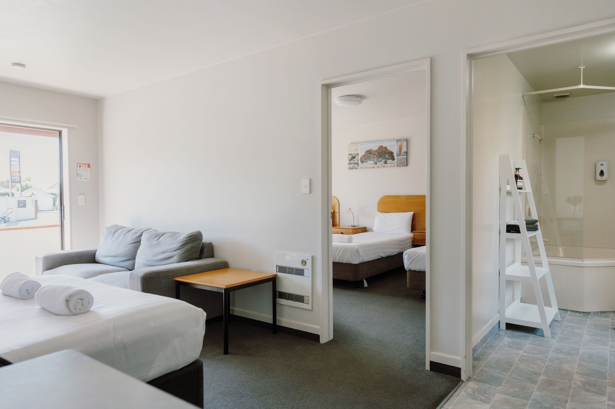 Habitació d'hotel amb dos llits, un sofà, una taula petita i zona de dutxa.