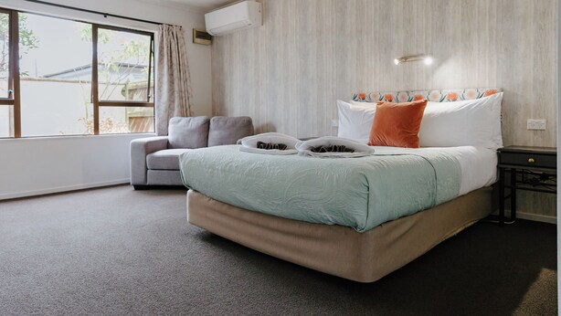 Quarto com cama grande, sofá cinza, janela com cortinas e ar condicionado fixado na parede.