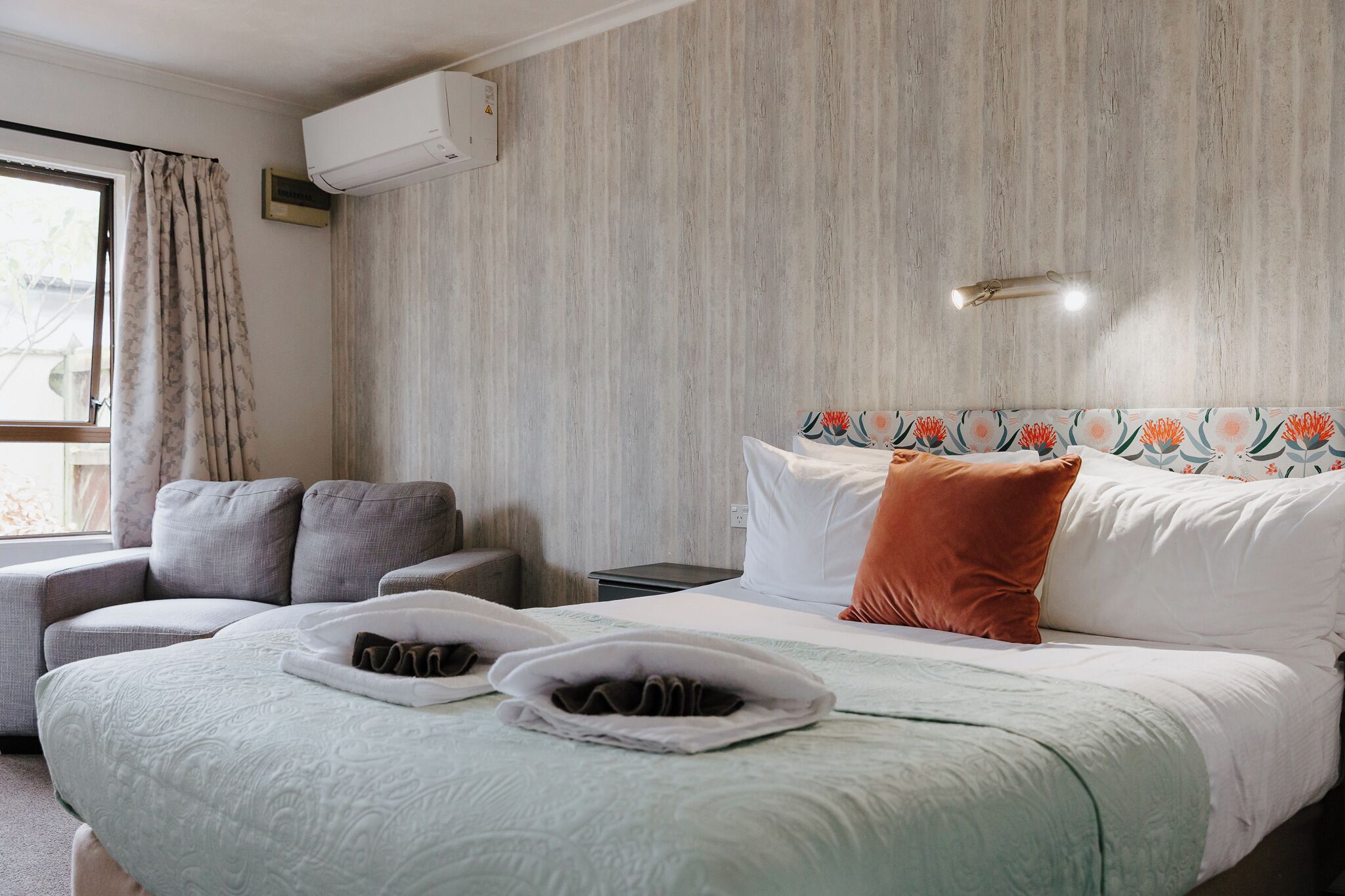 Una habitación de hotel con cama, sofá, mesita de noche y aire acondicionado.