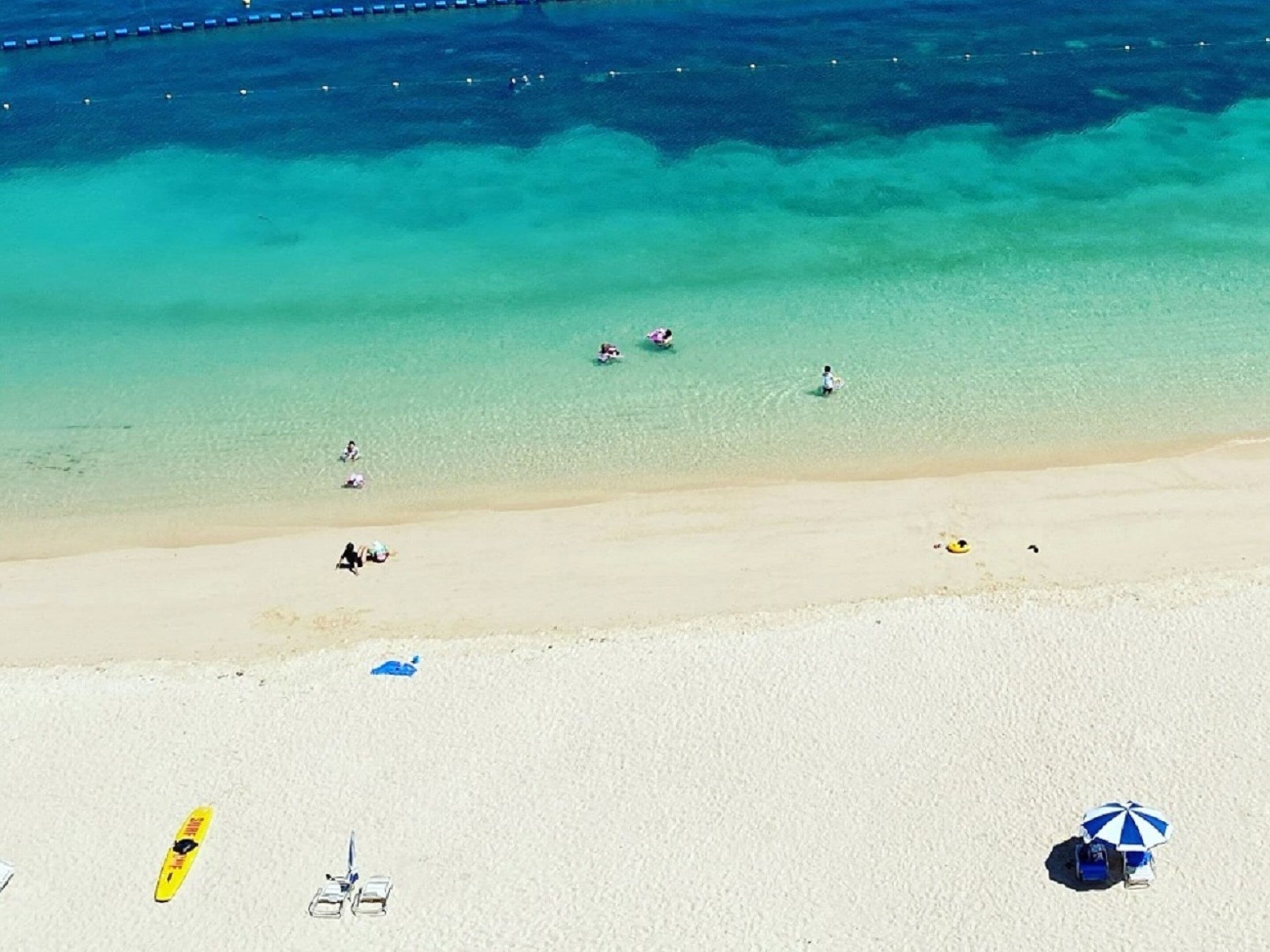 Een strand met helder turquoise water, een zandstrand en enkele badgasten.
