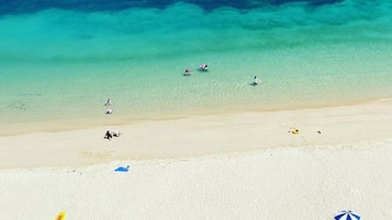 Een strand met helder turquoise water, een zandstrand en enkele badgasten.
