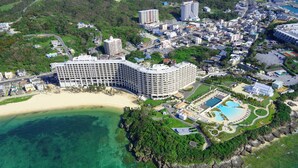 Vista aérea de um hotel à beira-mar, com vários edifícios e área de piscina.