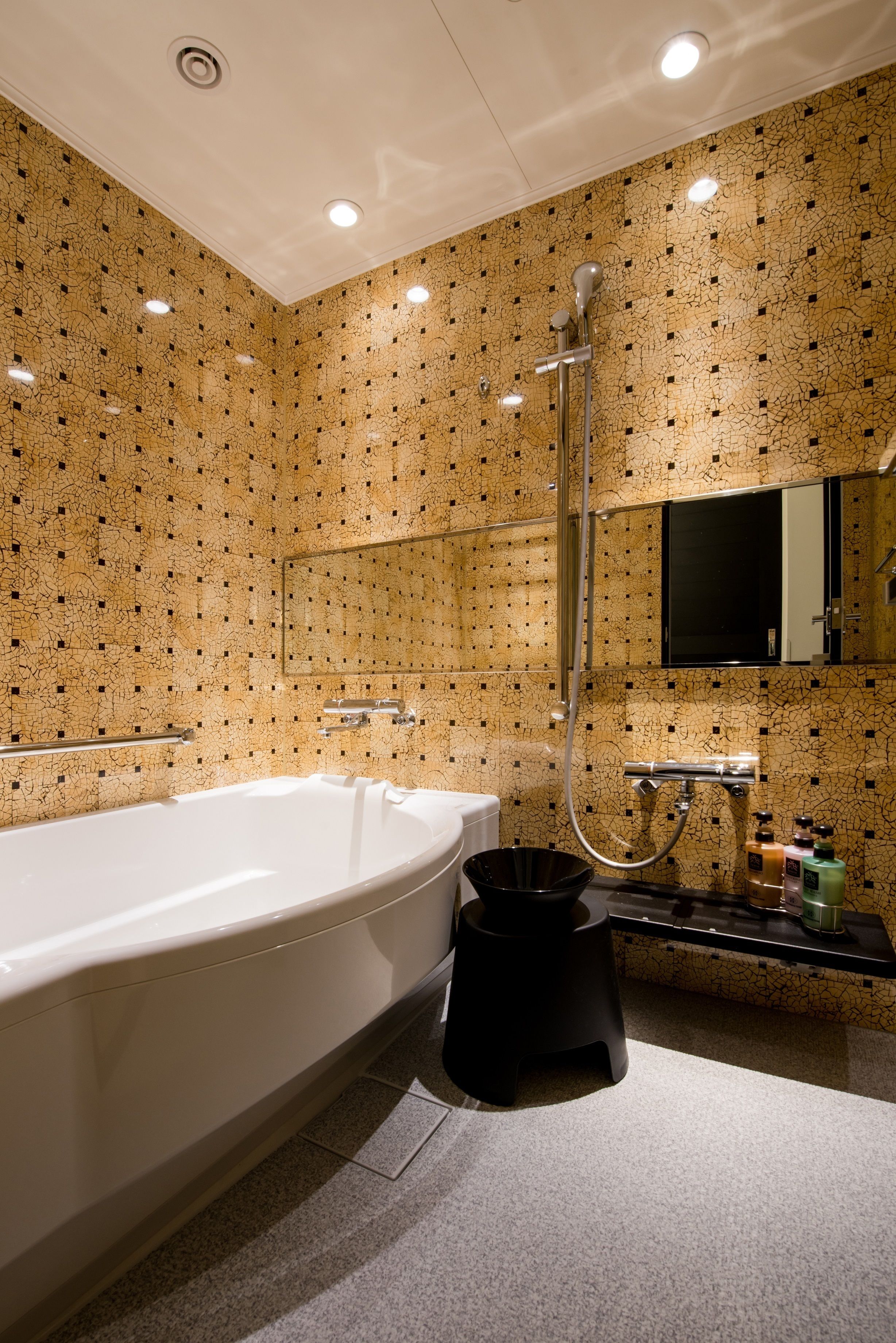 Un baño moderno con una bañera grande, un cabezal de ducha manual y un taburete negro.