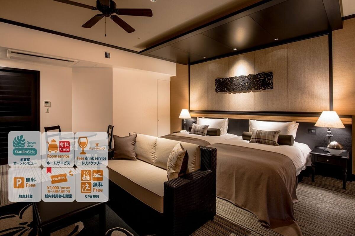Een hotelkamer met een bed, een bank, een kleine tafel, een aan de muur hangend kunstwerk en een plafondventilator.