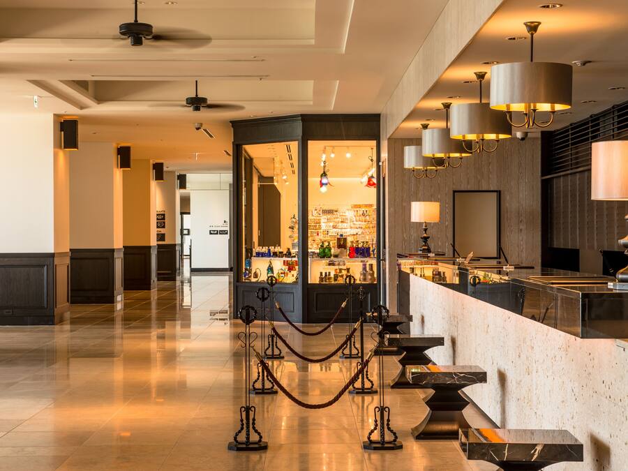 Un moderno vestíbulo de hotel con piso de mármol pulido, una zona de bar central con separador de vidrio e iluminación contemporánea.