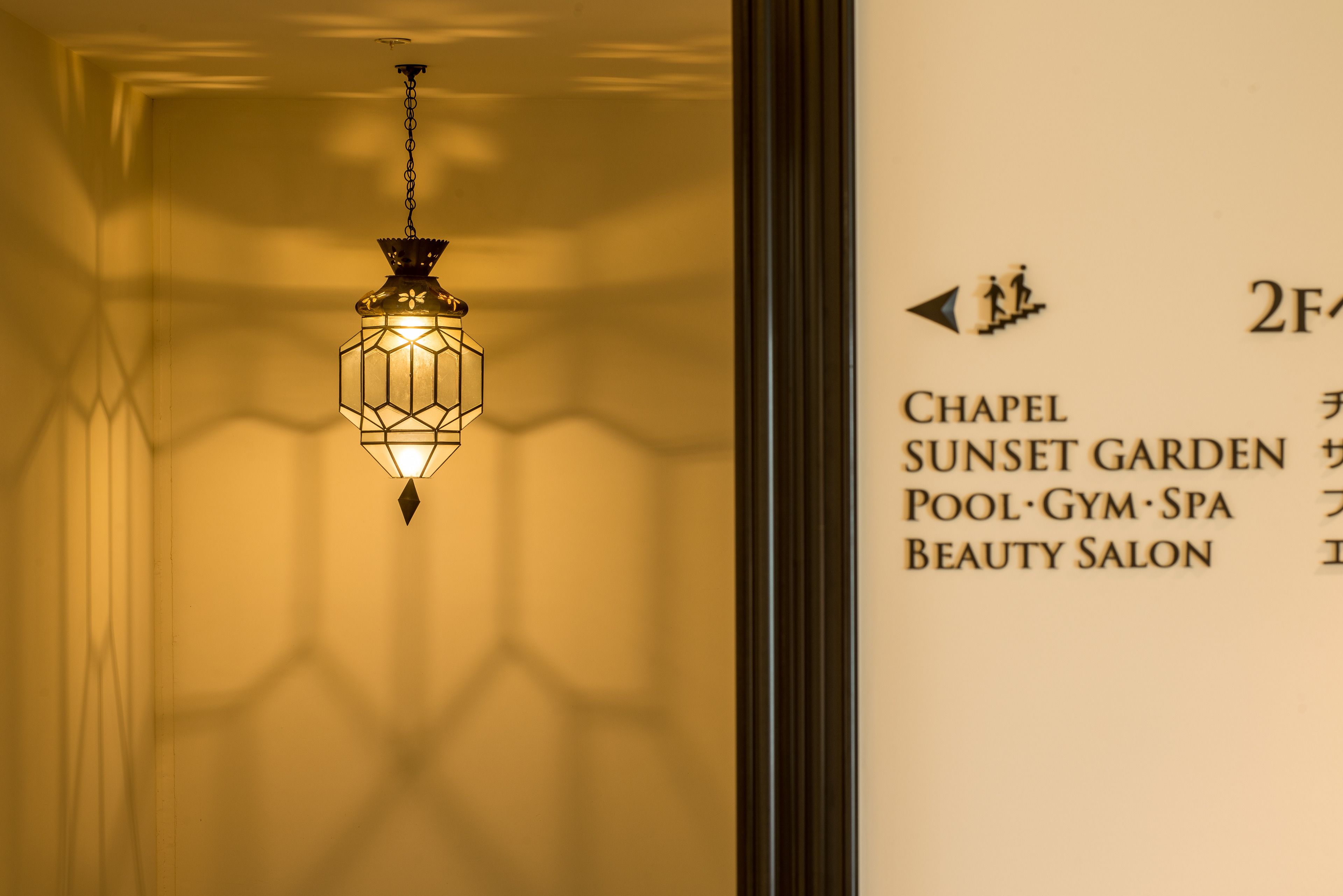 A hanging lantern with a geometric design, a wall with a list of amenities including a chapel, sunset garden, pool, gym, spa, and beauty salon.
