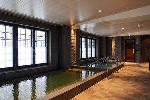 Ein moderner, überdachter Schwimmbereich mit großen Fenstern, einer Wand aus Naturstein und einem gefliesten Boden.