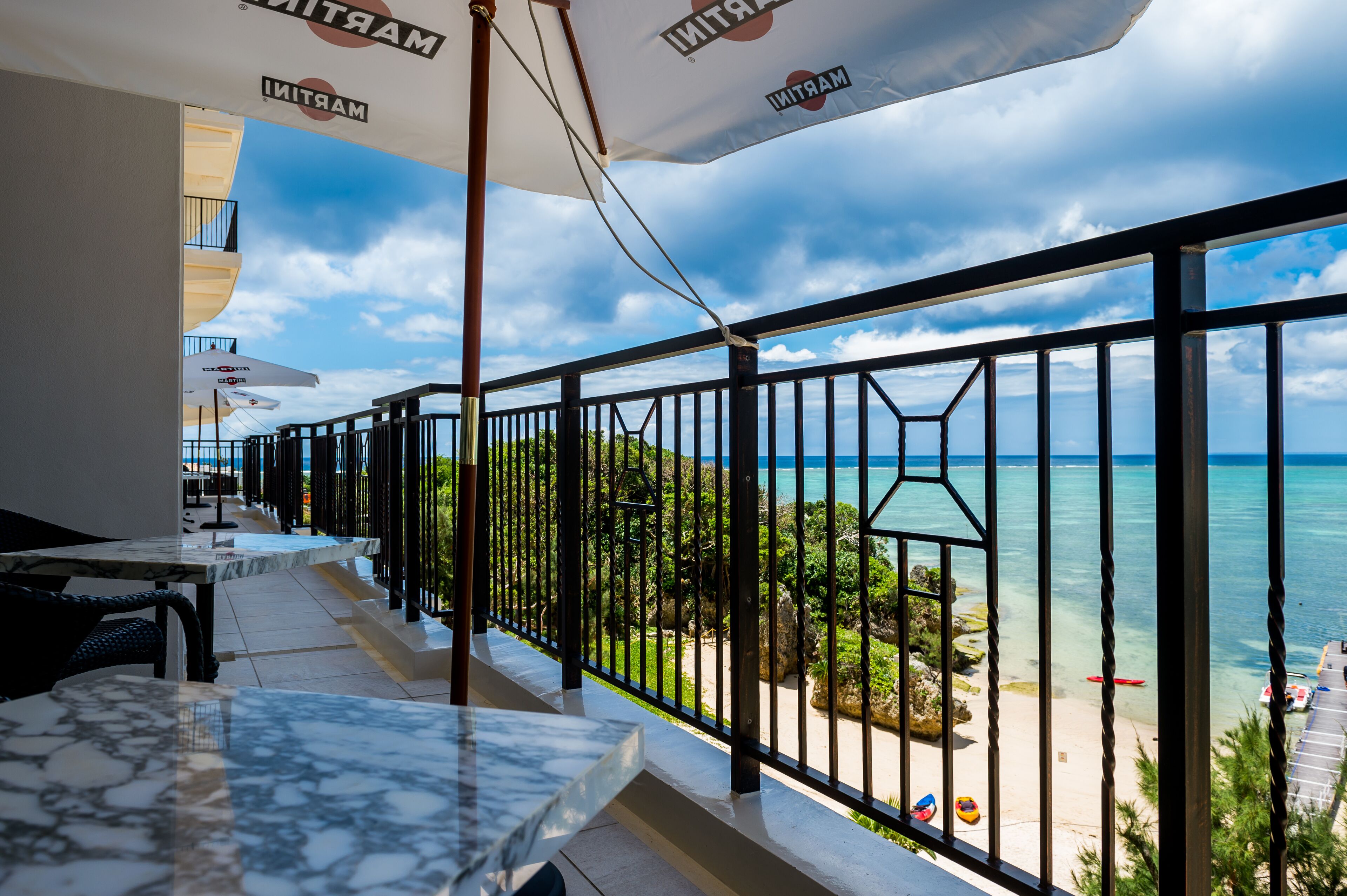 A balcony with a view of the ocean, equipped with outdoor seating and umbrellas.