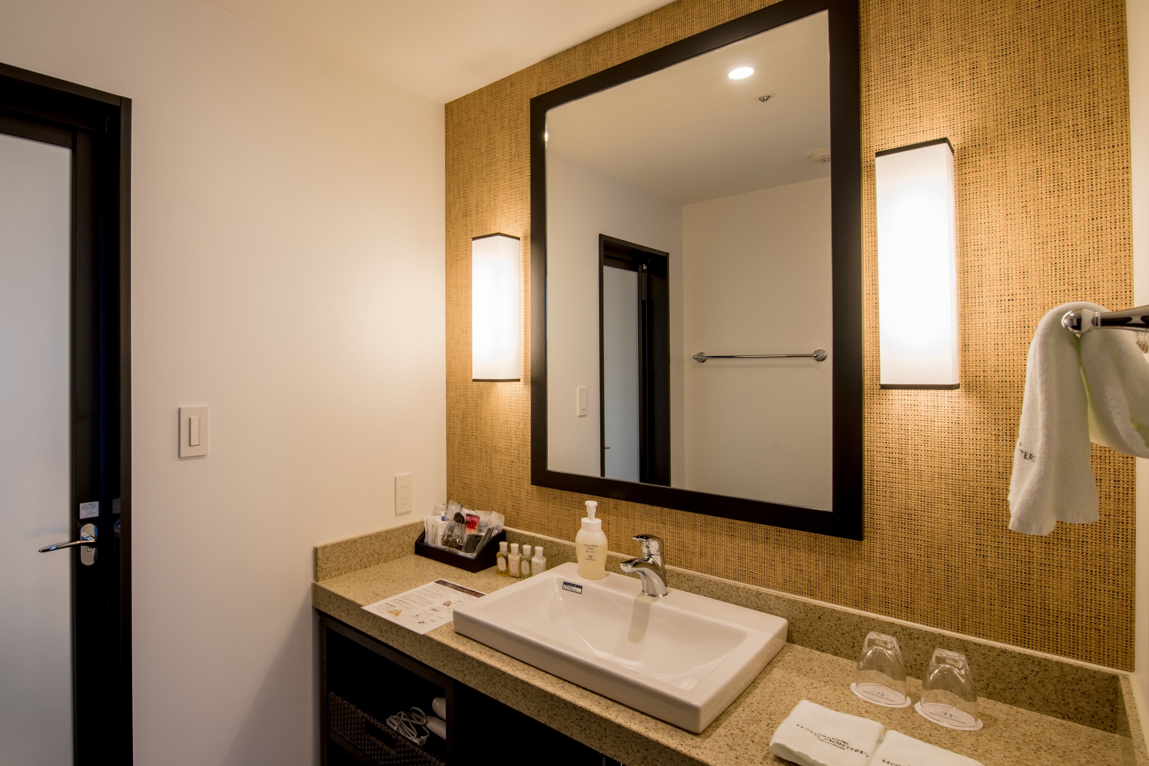 Un baño de hotel con un espejo grande, un lavamanos y un perchero para toallas.
