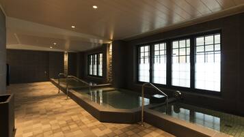 Une piscine intérieure moderne avec des murs en verre transparent, un sol à carreaux et un mur d’accent en pierre.