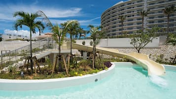 A water slide at a resort with a pool, palm trees, and a large building in the background.