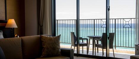 Habitación de hotel con sofá, una mesita y vista al océano a través de un ventanal corredero.