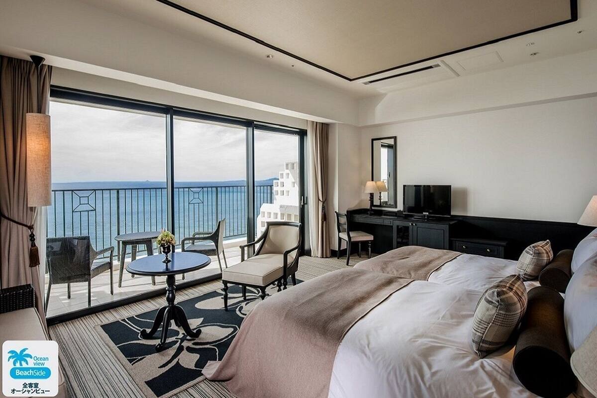 Een hotelkamer met een ruim balkon, een bed, een bureau en een televisie.